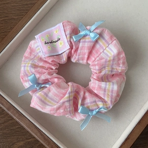 Detailed close-up of pink plaid scrunchie with blue bows and a handmade fabric label
