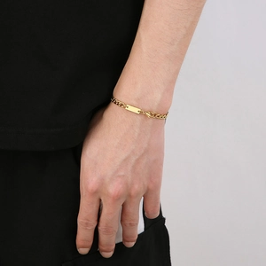 Detailed view of a gold Cuban chain bracelet with a polished rectangular tag on the wrist