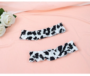 Detail of cow print elastic leg garters with ruffled edges on pink fabric background