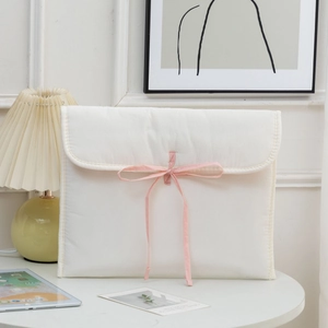 Quilted off-white 13 inch laptop sleeve with soft pink ribbon bow on a white table