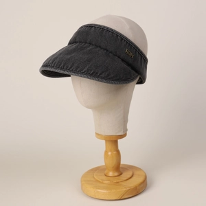 Detailed macro view of dark grey denim sun visor cap with decorative gold metal emblem