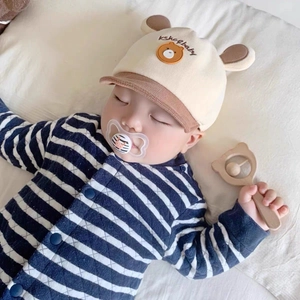Détail du bonnet de bébé ours avec barboteuse rayée et hochet en bois sur lit doux