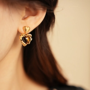 Close-up of heart-shaped gold earrings with tiger eye stone on a model's ear