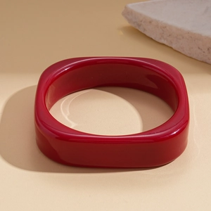 Detail view of bold red resin geometric square bangle on a textured neutral background