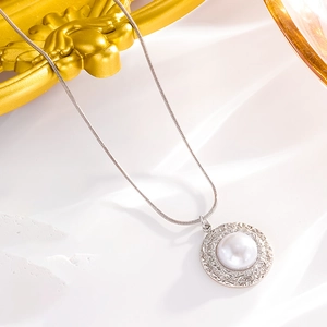 Macro shot of silver snake chain with round vintage textured pearl pendant on marble