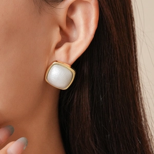 Close-up of model wearing geometric square pearl studs with textured gold frame