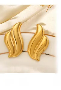 Golden flame wave stud earrings displayed on a white ceramic plate with dried flowers