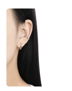Detailed view of silver gear-shaped ear cuff and sleek earring on human ear