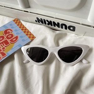 Macro shot of stylish white cat-eye sunglasses with dark lenses on soft white fabric