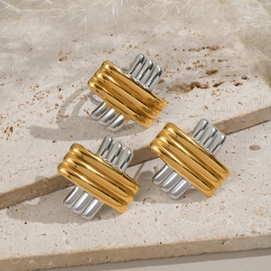 Minimalist gold and silver striped cross earrings on a beige travertine stone surface