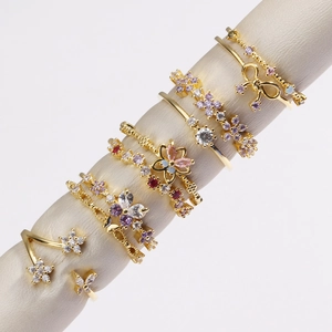 Détail de bagues plaquées or avec zircons roses et mauves en forme de fleurs et papillons