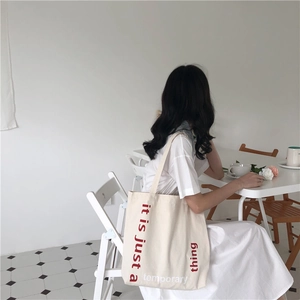 Close-up of cream canvas tote bag with red text print in a minimalist cafe setting