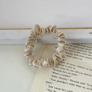 Macro detail of champagne satin scrunchie with silk texture on vintage book page