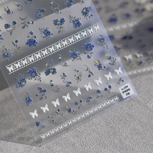 Détail macro de stickers 3D pour ongles avec fleurs bleues et motifs de papillons blancs