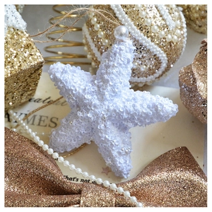 Close-up of white sequined star ornament with pearl pendant on golden festive background