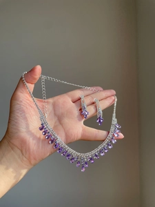 Macro shot of silver-plated necklace and drop earrings set with purple teardrop crystals
