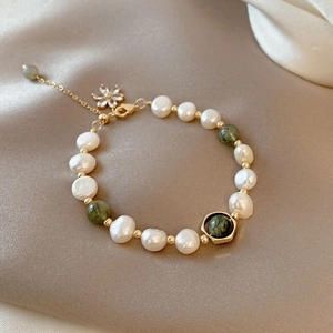 Detailed shot of irregular pearls and green beads with a golden flower charm on silk