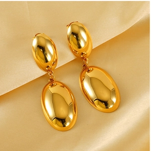 Close-up of gold oval drop earrings with mirror finish on champagne silk background