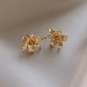 Macro detail of matte gold floral earrings with textured petals on silk fabric