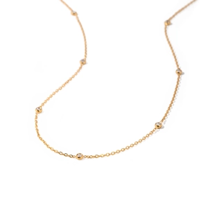 Detail of a thin gold necklace with multiple round gemstones on a clean white background