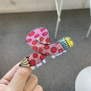 Pink acrylic pencil hair claw clip with red polka dots shown held by hand