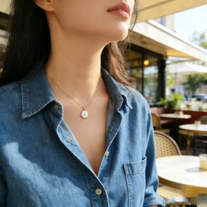 Primo piano di una collana dorata con ciondolo a cuore esagonale bianco su modella in denim