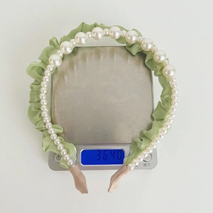 Detailed top view of light green pleated satin headband with pearls on scale weighing 36g