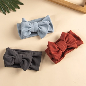 Detail view of three knit baby headbands with oversized bows in blue, red, and grey tones