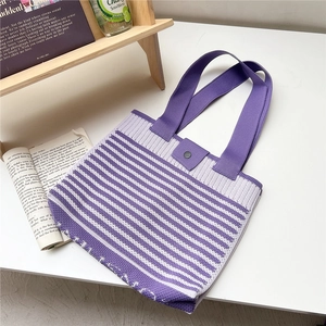Flat lay of purple striped knit tote bag with snap button and dual handles on a desk