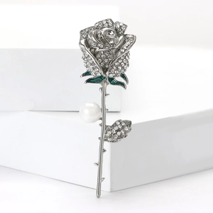 Detail of rose brooch with white rhinestones, green enamel leaves and a central pearl