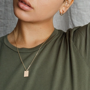 Detail of double-layer gold necklace with rectangular pendant and hoop earrings