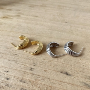 Detailed close-up of textured gold and silver arc hoop earrings on wooden background