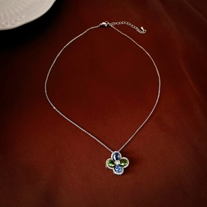 Elegant silver necklace with clover pendant featuring blue and green gems on velvet