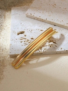 Detail view of double-bar gold metal hair clip on beige travertine and sand