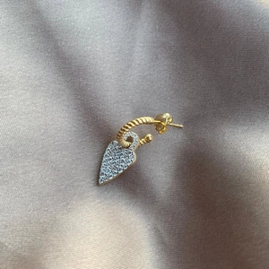 Macro shot of gold twist hoop earring with sparkling heart pendant on silk background