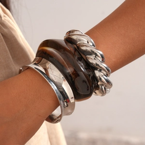 Close-up of stacked metallic silver bangles and amber resin bracelet on model's wrist