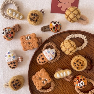 Flat lay of wool felt strawberry and food-shaped hair ties on white fabric and wooden tray