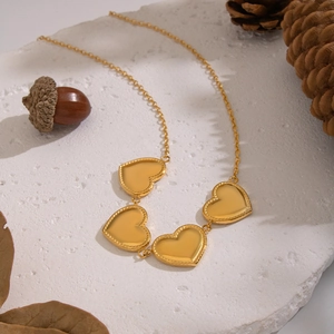 Dettaglio della collana dorata con più cuori su pietra bianca con foglie autunnali secche
