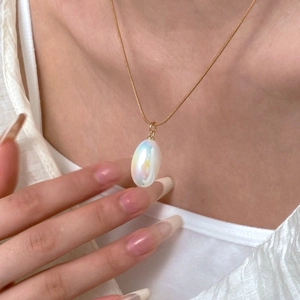 Close-up of a gold necklace with an iridescent pearly pear-shaped teardrop pendant