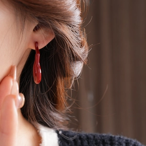 Macro side view of model wearing deep red resin teardrop earrings in fluid lava design