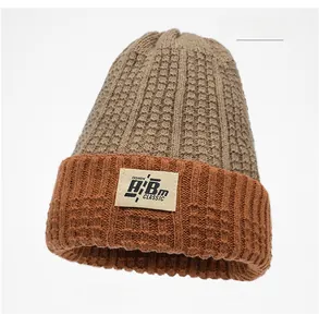 Dettaglio del cappello in maglia bicolore kaki e caramello con etichetta tessuta a lettere