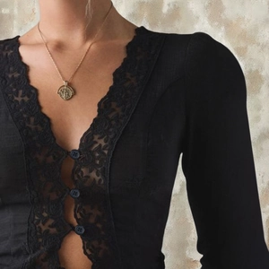 Détail du décolleté en V avec broderie de dentelle noire raffinée et petits boutons