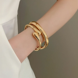 Close-up of a glossy gold droplet-shaped cuff bracelet on a model wrist for a chic style