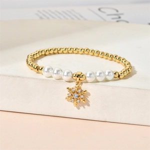 Close-up of golden beaded bracelet with pearl accents and snowflake pendant