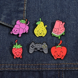 Set of six colorful fruit-themed cat enamel pins displayed on blue denim fabric background