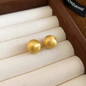 Macro shot of gold brushed round stud earrings resting on a beige velvet jewelry box