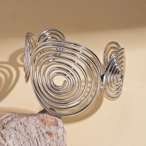 Macro detail of a silver spiral cuff bracelet resting on a stone with artistic shadows