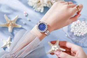 Detailed view of silver mesh band watch with diamond-encrusted blue dial on wrist