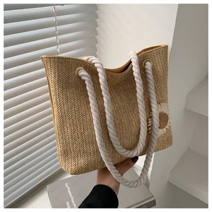 Detail of woven straw tote bag featuring a white daisy patch and thick cotton rope handle