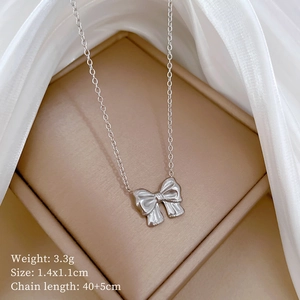 Detailed view of a silver bow pendant necklace on white silk fabric with dimensions
